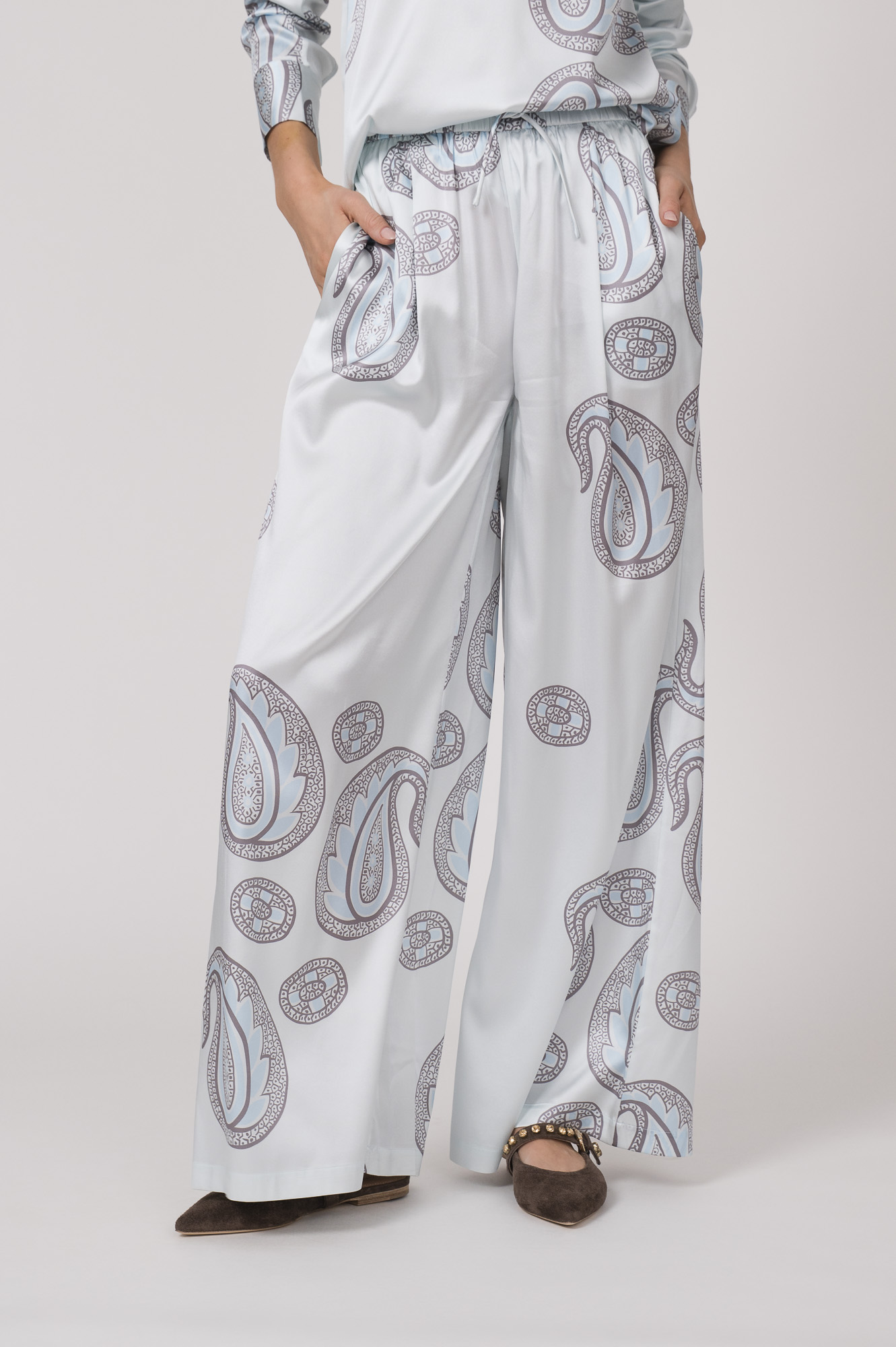 Model trägt eine fließende Hose in hellem Blau mit Paisley Muster der Marke Herzens.