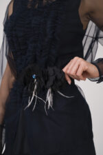 Model trägt ein Outfit der Marke Susanne Bommer in marine-blau bestehend aus: einem ärmellosem Seidentop, einer durchsichtige Tüllbluse, einem Federgürtel.