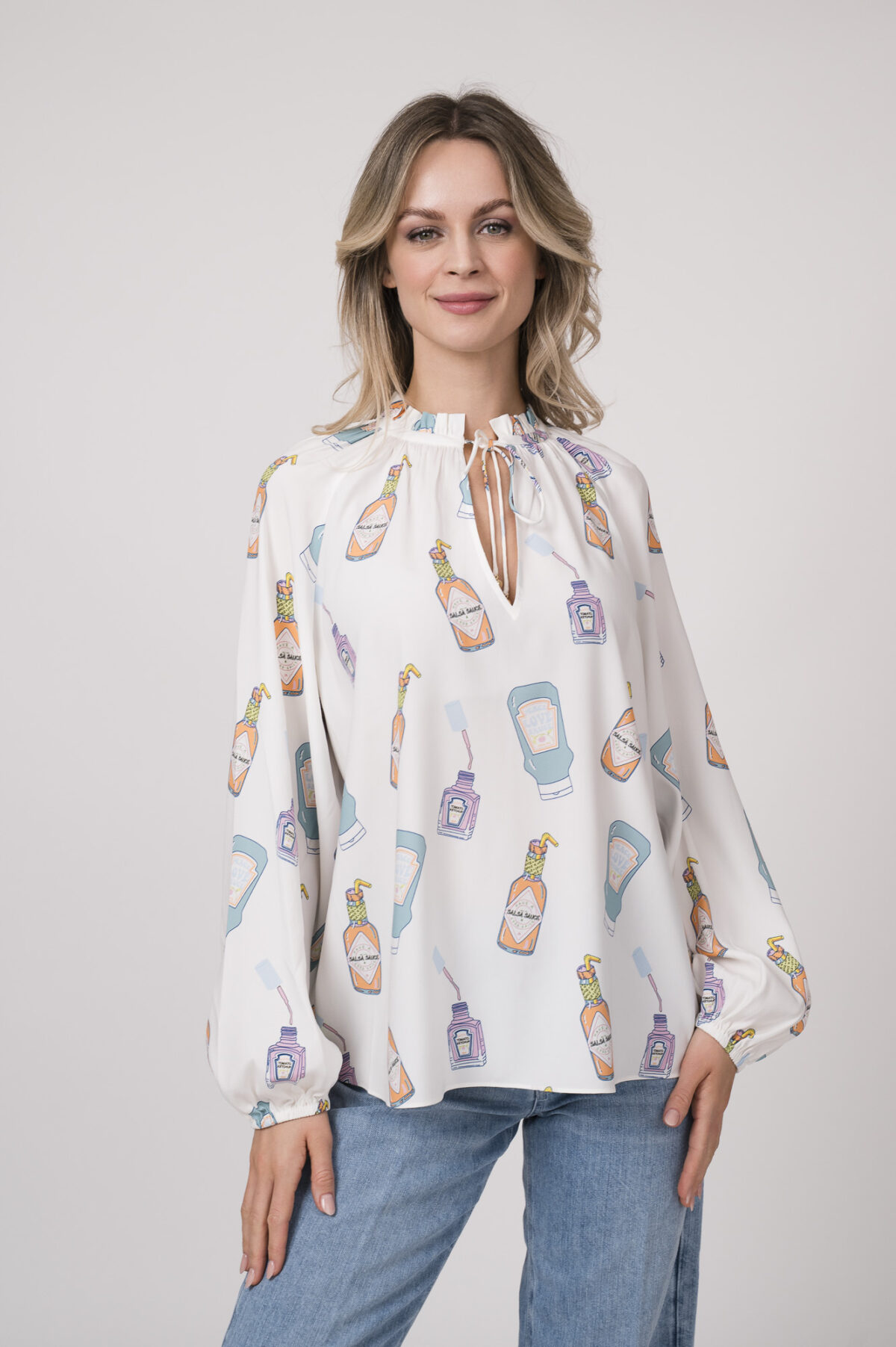 Model trägt eine weiße Bluse mit Flaschen-Muster der Marke Herzens.