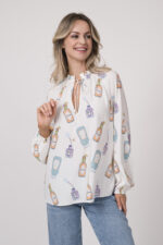 Model trägt eine weiße Bluse mit Flaschen-Muster der Marke Herzens.