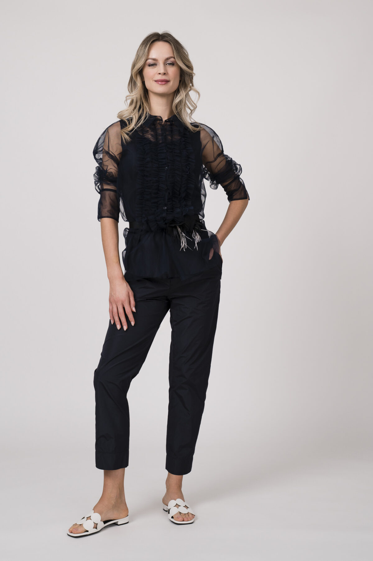 Model trägt ein Outfit der Marke Susanne Bommer in marine-blau bestehend aus: ärmellosem Seidentop, Stoffhose, durchsichtige Tüllbluse, Federgürtel.