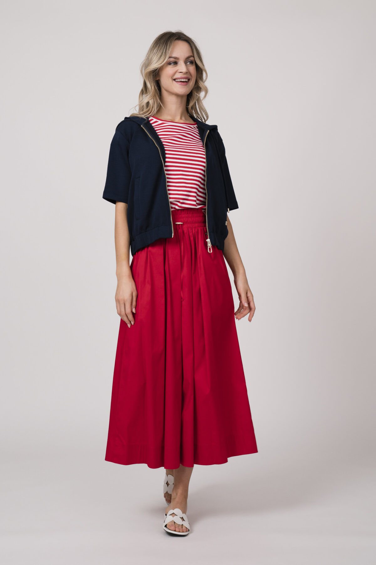 Model trägt einen dunkelblauen Kurzarm-Sweater mit Reißverschluss, ein rot-weiß gestreiftes Shirt, einen roten Rock - alles von der Marke Joop!