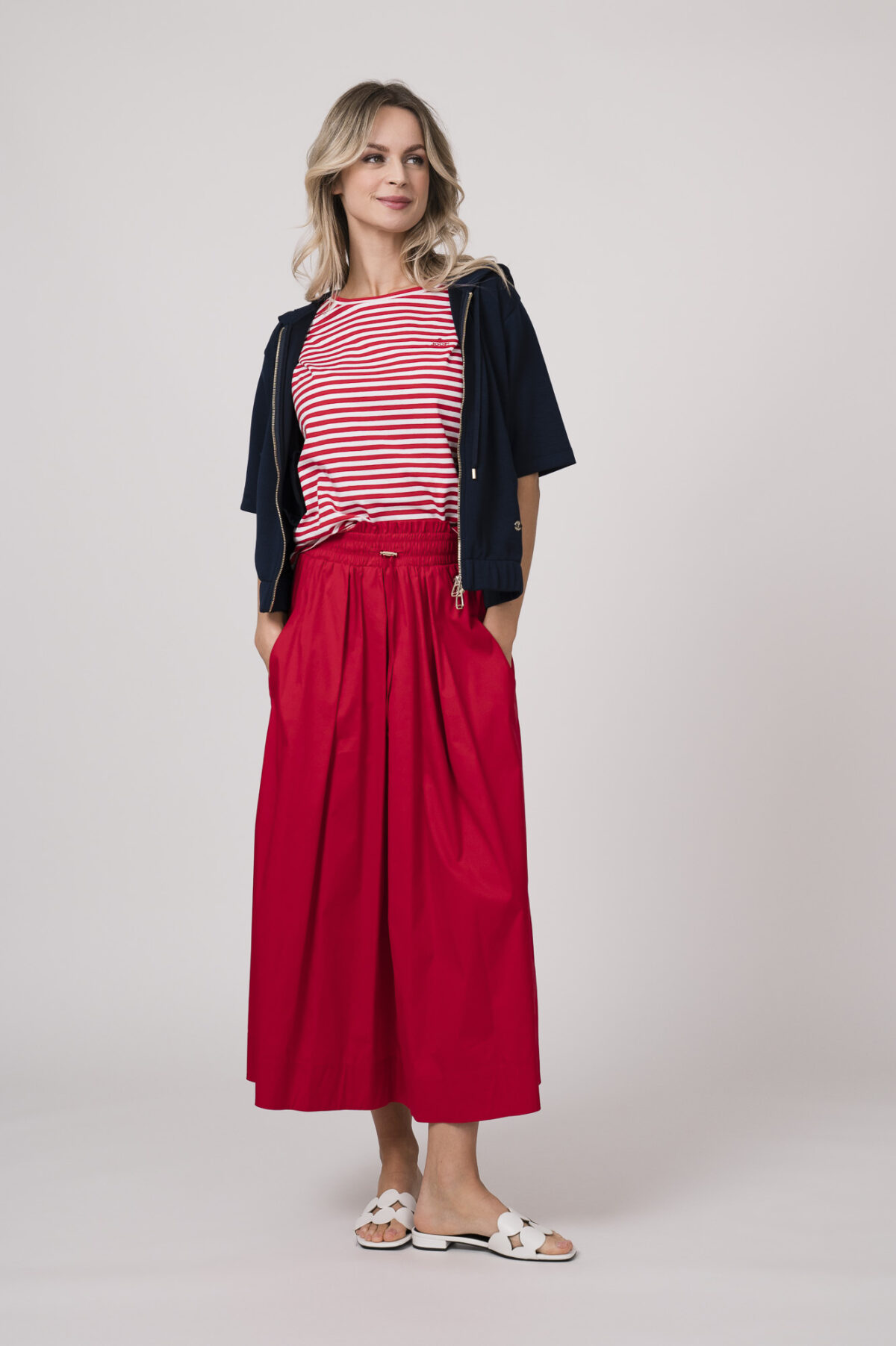 Model trägt einen dunkelblauen Kurzarm-Sweater mit Reißverschluss, ein rot-weiß gestreiftes Shirt, einen roten Rock - alles von der Marke Joop!