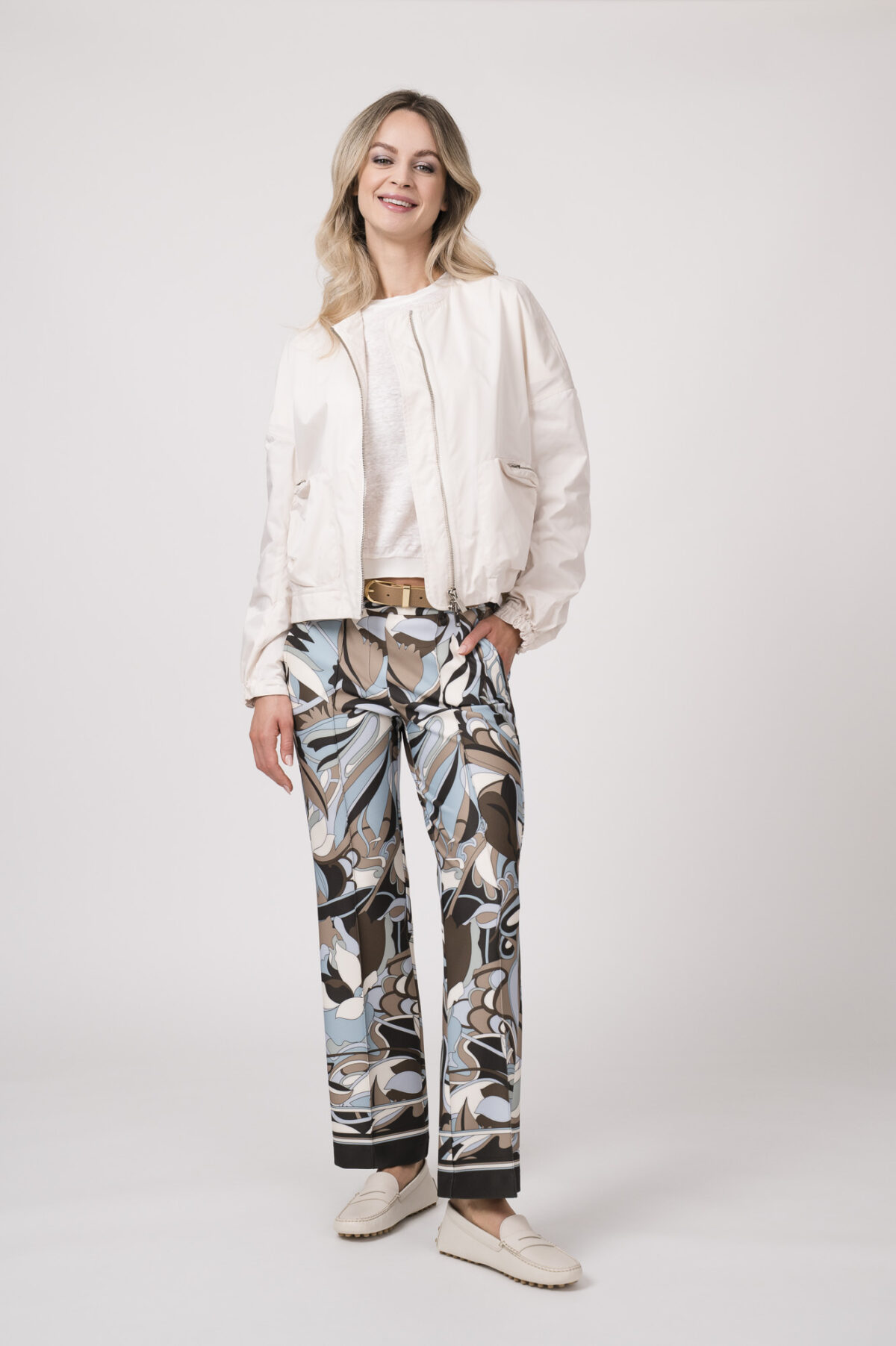 Model trägt eine Jacke der Marke Lis Lareida in Natur, ein Shirt der Marke Dorothee Schumacher in Weiß aus 100 % Hanf, dazu eine gemusterte Hose der Marke Cambio und einen Gürtel in Beige der Marke Aigner.