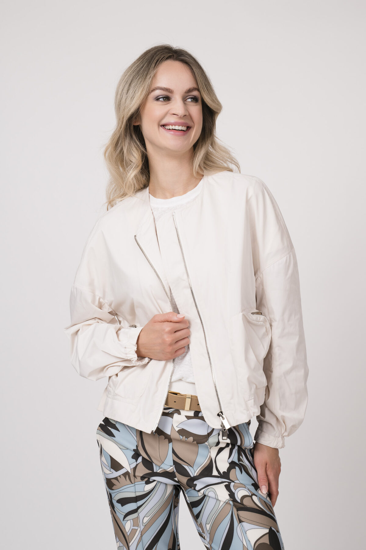 Model trägt eine Jacke der Marke Lis Lareida in Natur, ein Shirt der Marke Dorothee Schumacher in Weiß aus 100 % Hanf, dazu eine gemusterte Hose der Marke Cambio und einen Gürtel in Beige der Marke Aigner.