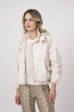 Model trägt eine Jacke der Marke Mabrun in Natur mit goldfarbenen Druckknöpfen. Dazu trägt sie eine gemusterte Hose der Marke Cambio und einen Kurzarmpullover der Marke FFC in Weiß.