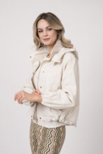 Model trägt eine Jacke der Marke Mabrun in Natur mit goldfarbenen Druckknöpfen. Dazu trägt sie eine gemusterte Hose der Marke Cambio und einen Kurzarmpullover der Marke FFC in Weiß.