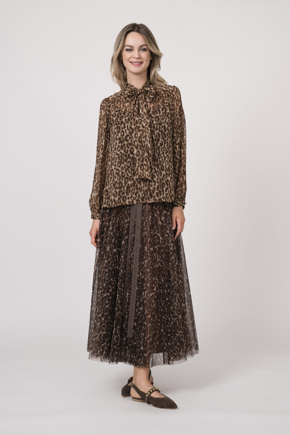 Model trägt eine Bluse mit Schnuppe der Marke Joop! und einen dazu passenden Plisseerock der Marke Joop!. Beides in einem Leo-Muster.