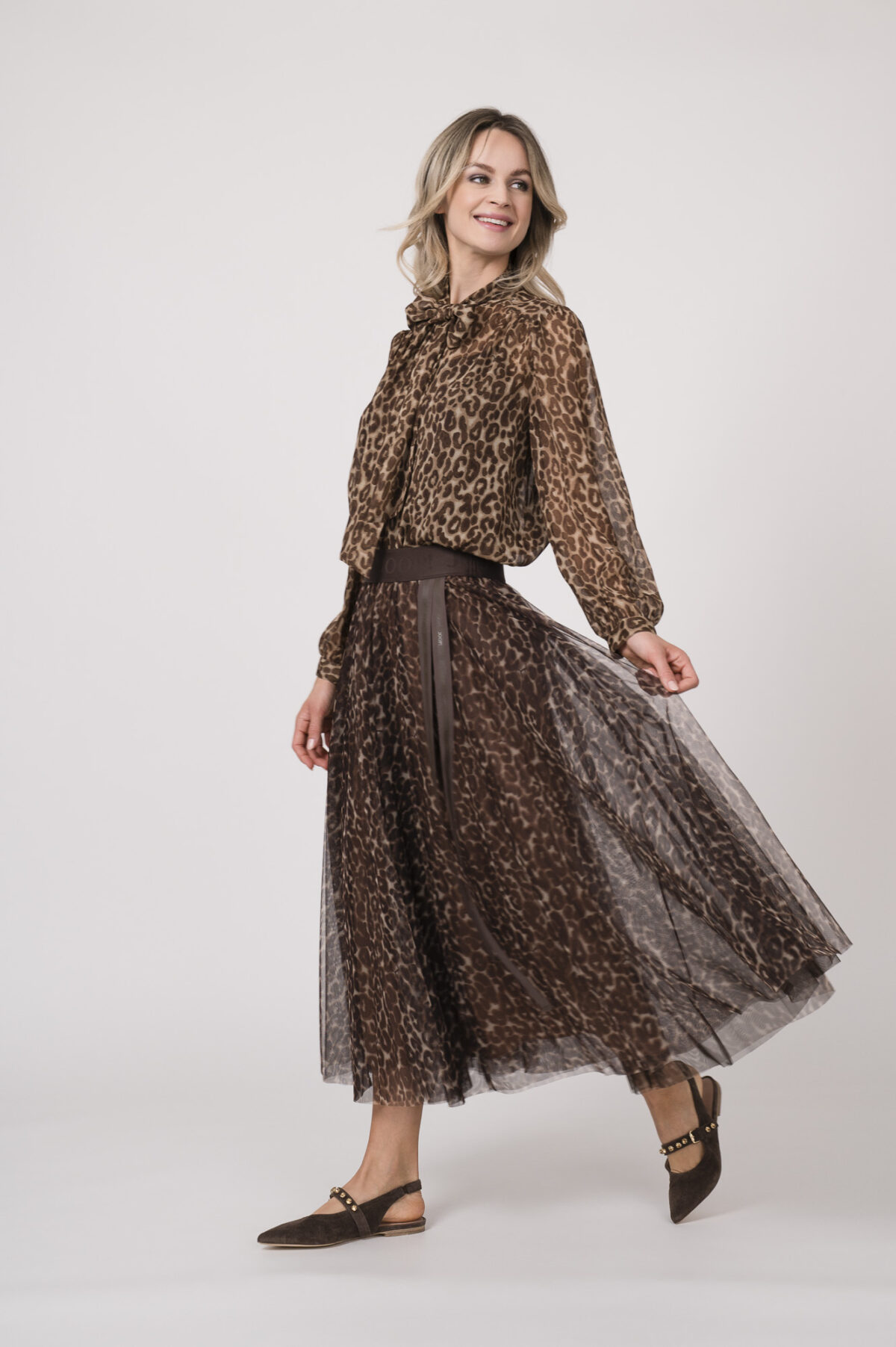 Model trägt eine Bluse mit Schnuppe der Marke Joop! und einen dazu passenden Plisseerock der Marke Joop!. Beides in einem Leo-Muster.