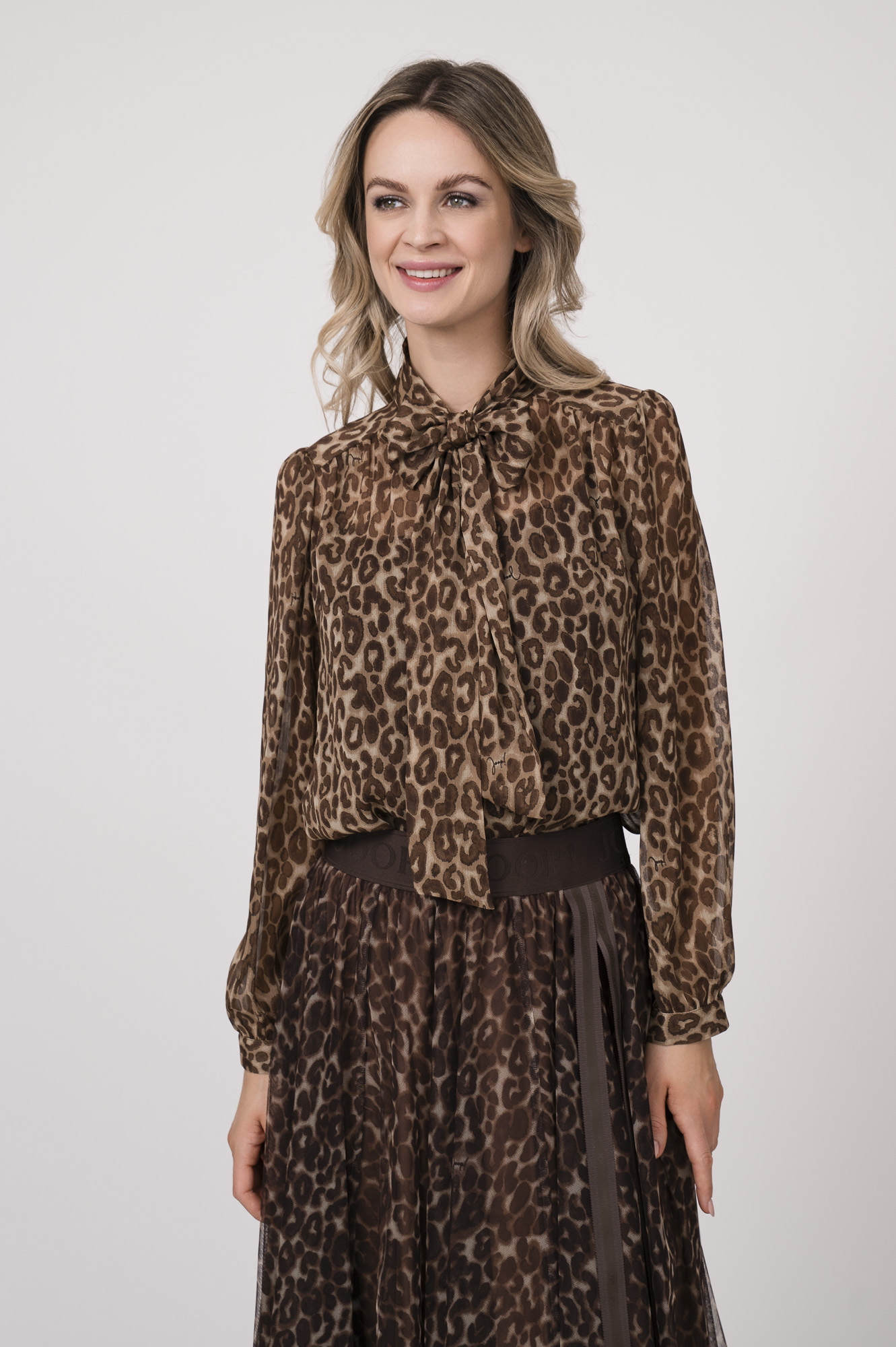 Model trägt eine Bluse mit Schnuppe der Marke Joop! und einen dazu passenden Plisseerock der Marke Joop!. Beides in einem Leo-Muster.