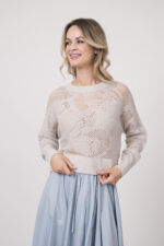 Model trägt einen Langarmpullover in der Farbe Sand der Marke Herzens, dazu einen Rock der Marke FFC in Hellblau.