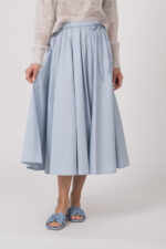 Model trägt einen Langarmpullover in der Farbe Sand der Marke Herzens, dazu einen Rock der Marke FFC in Hellblau.