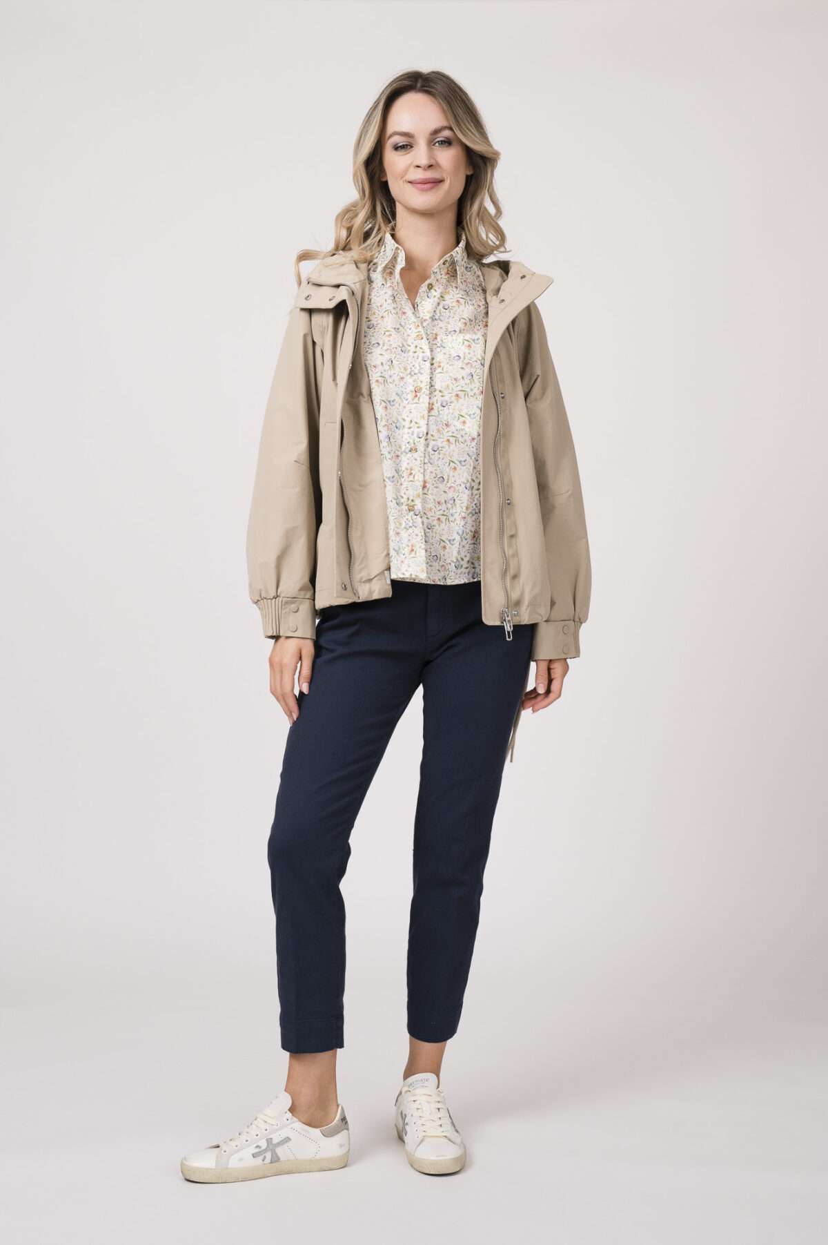 Model trägt eine Jacke der Marke Duno in der Farbe Sand. Eine Bluse der Marke Rossana Diva mit Blumenmuster. Dazu eine Hose der Marke Mason's in Marine.