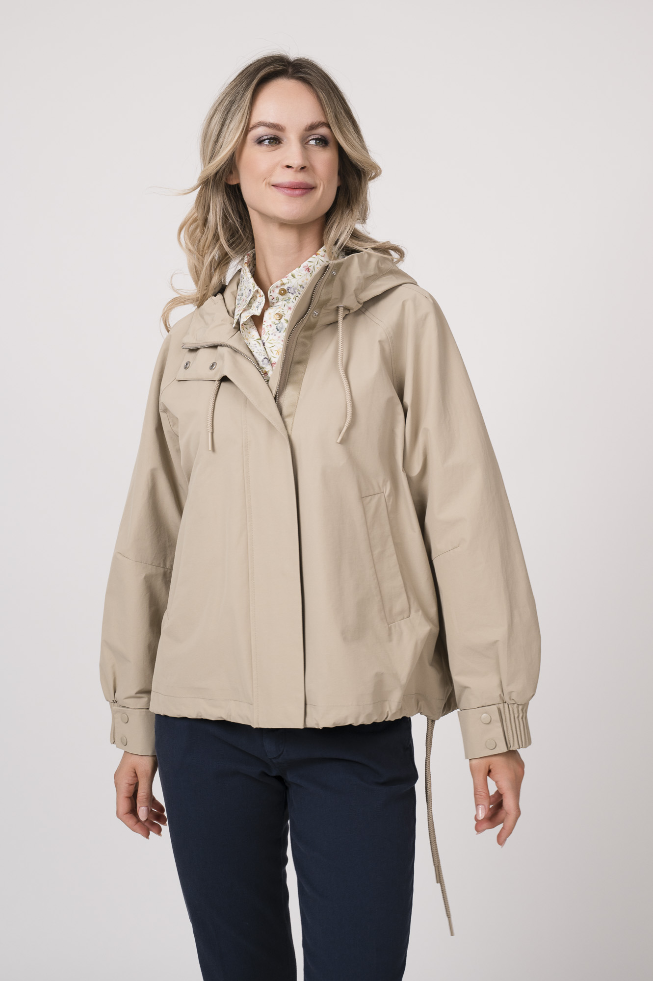 Model trägt eine Jacke der Marke Duno in der Farbe Sand. Eine Bluse der Marke Rossana Diva mit Blumenmuster. Dazu eine Hose der Marke Mason's in Marine.