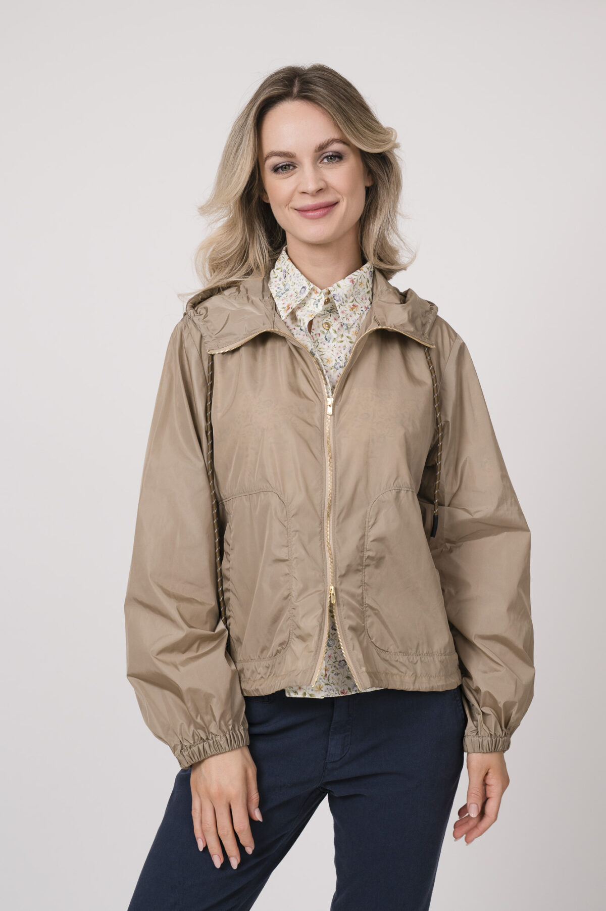 Model trägt eine Jacke der Marke Lis Lareida in der Farbe Sand. Eine Bluse der Marke Rossana Diva mit Blumenmuster. Dazu eine Hose der Marke Mason's in Marine.