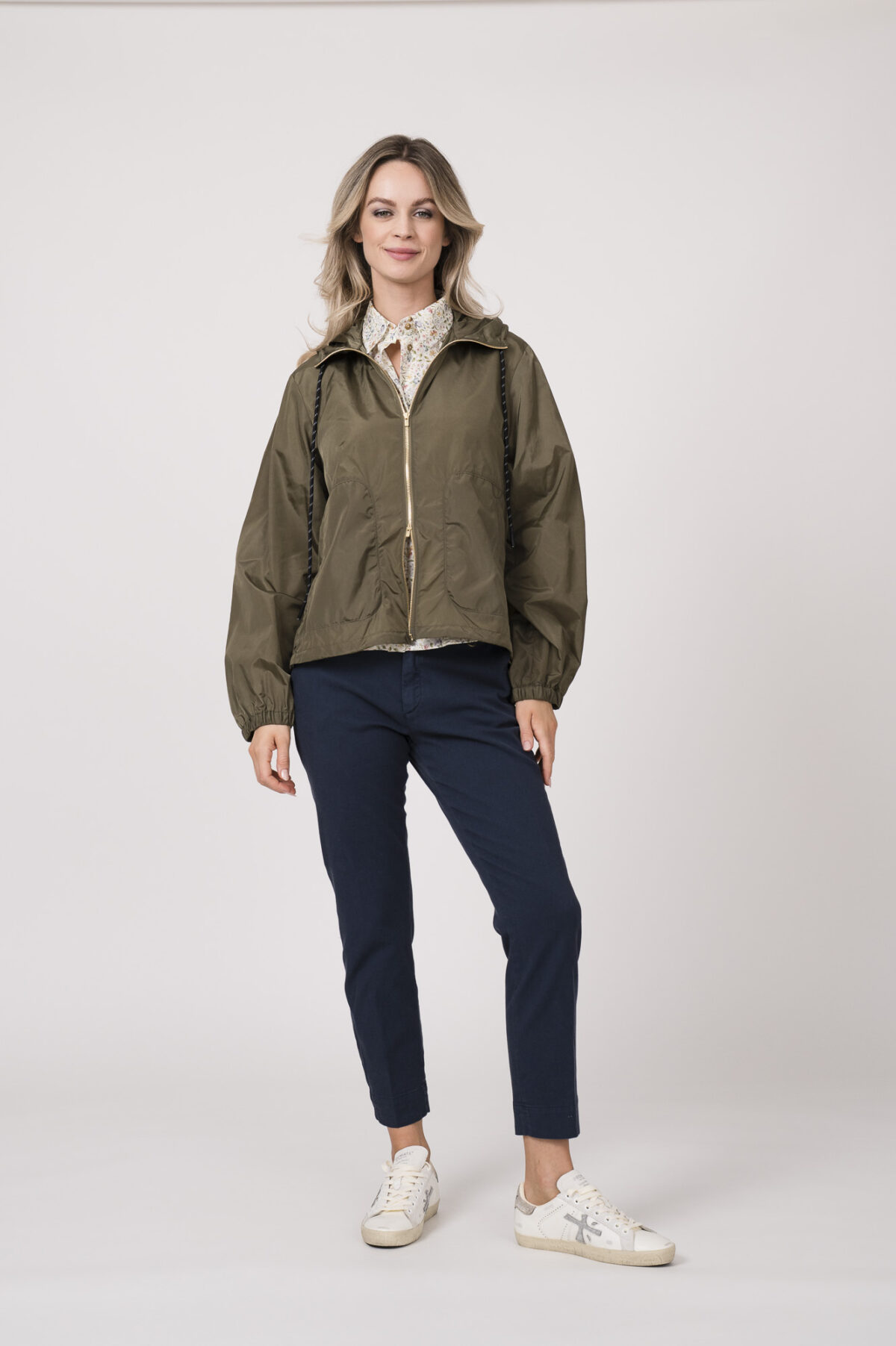 Model trägt eine Jacke der Marke Lis Lareida in der Farbe Sand. Eine Bluse der Marke Rossana Diva mit Blumenmuster. Dazu eine Hose der Marke Mason's in Marine.