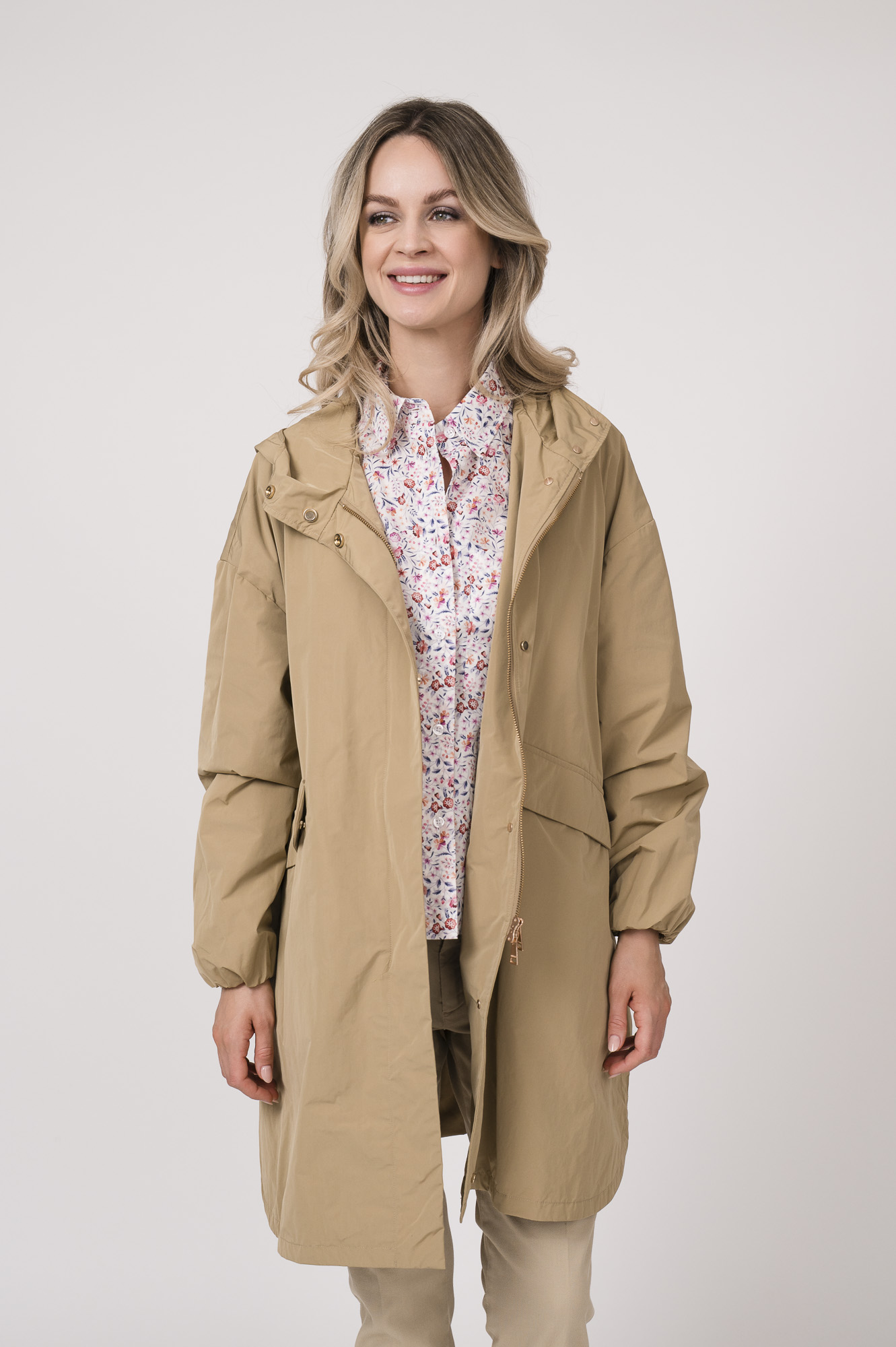 Model trägt einen Mantel der Marke Mabrun in der Farbe Camel. Eine Bluse der Marke Rossana Diva mit Blumenmuster. Dazu eine Hose der Marke Mason's in der Farbe Sand.