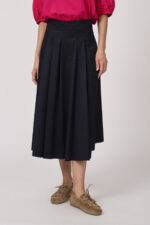 Model trägt eine Bluse der Marke Susanne Bommer in der Farbe Pink, dazu einen Rock der Marke Susanne Bommer in Marine. Einen Gürtel mit Federn der Marke Susanne Bommer.