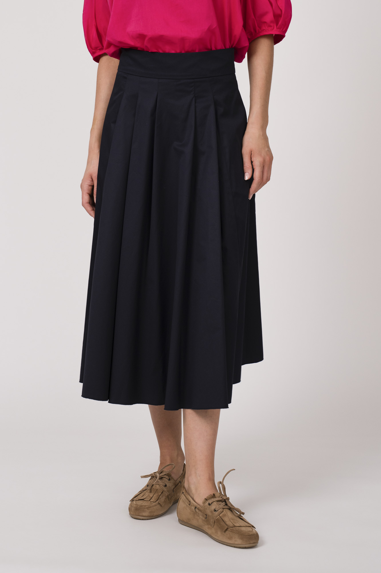 Model trägt eine Bluse der Marke Susanne Bommer in der Farbe Pink, dazu einen Rock der Marke Susanne Bommer in Marine. Einen Gürtel mit Federn der Marke Susanne Bommer.