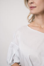 Model trägt eine Bluse der Marke Susanne Bommer in der Farbe Weiß, dazu einen Rock der Marke Susanne Bommer in Marine.