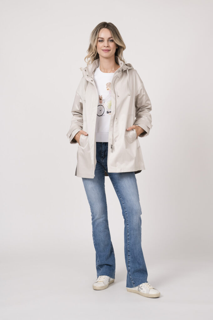Model trägt einen Lounge-Sweater der Marke Sustyle in Weiß mit Motiv in Pink auf der Vorderseite. Dazu eine Jeans der Marke 7 for all mankind in Mittelblau. Eine Jake der Marke Duno in der Farbe Champagner.
