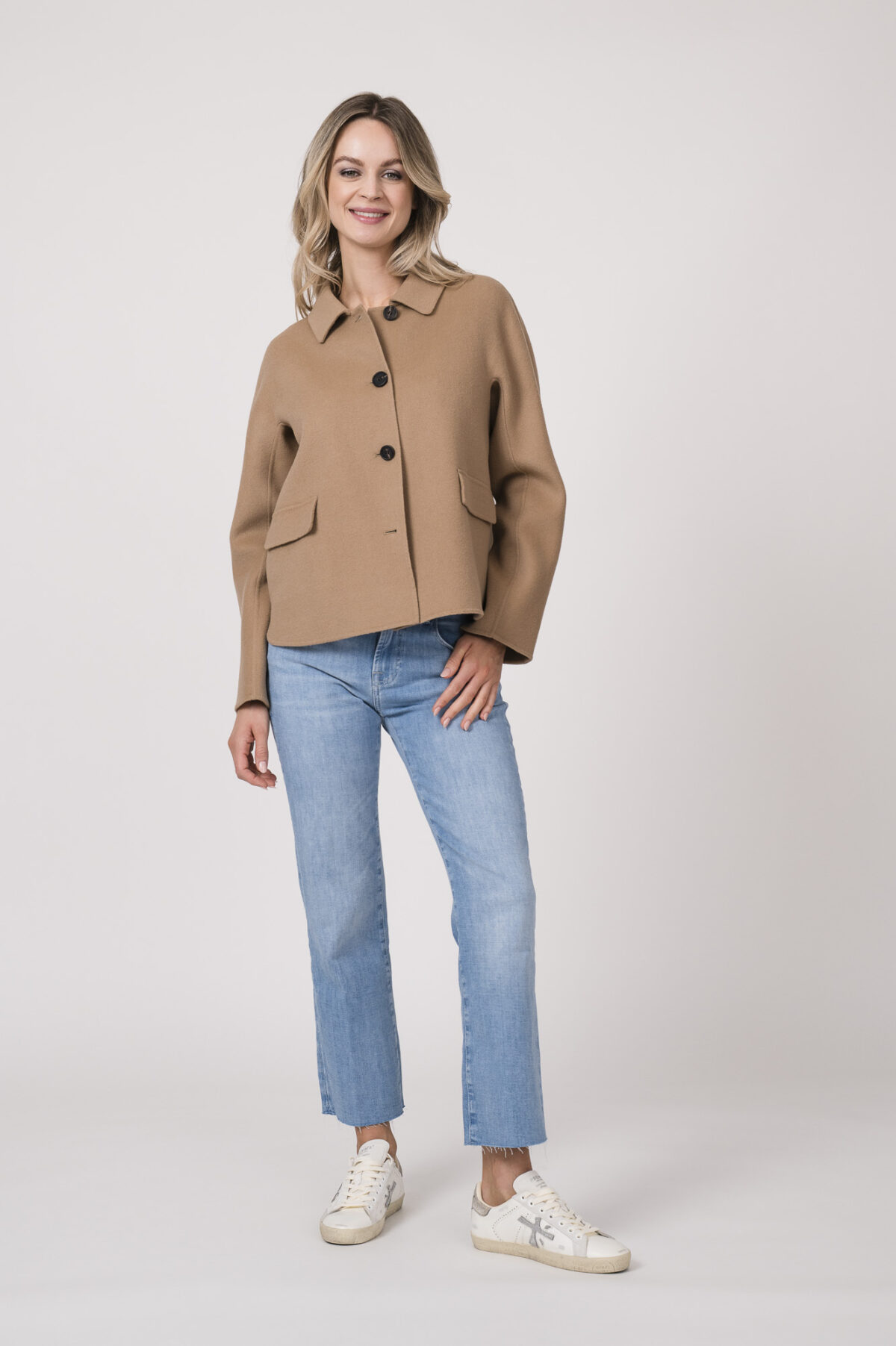 Model trägt einen Kurzarmpulli der Marke Joop! in Weiß, eine Jeans der Marke 7 for all mankind in hellblau. Eine Jacke der Merke Mabrun in Camel.