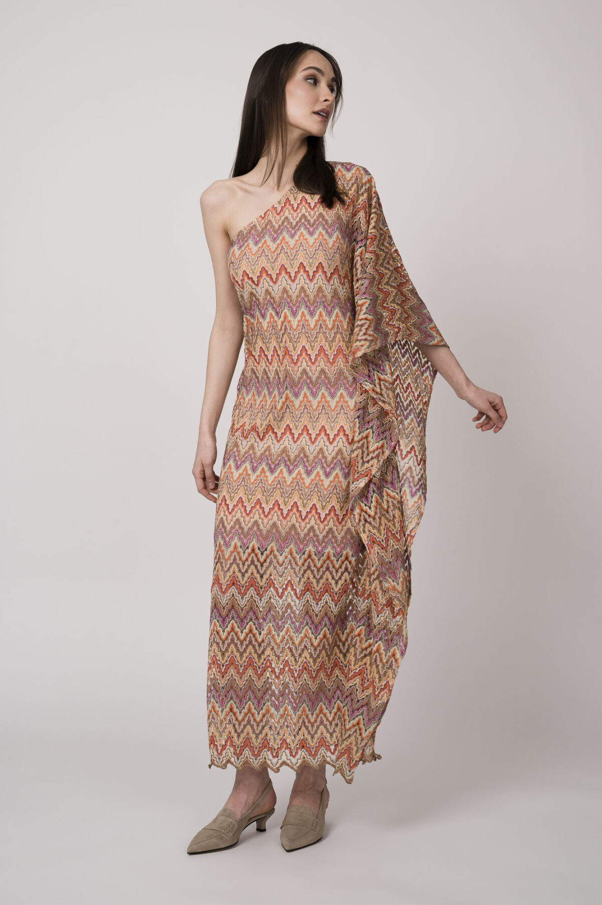 Model trägt ein oranges gemustertes, asymmetrisches Strickkleid von Ana Alcazar.