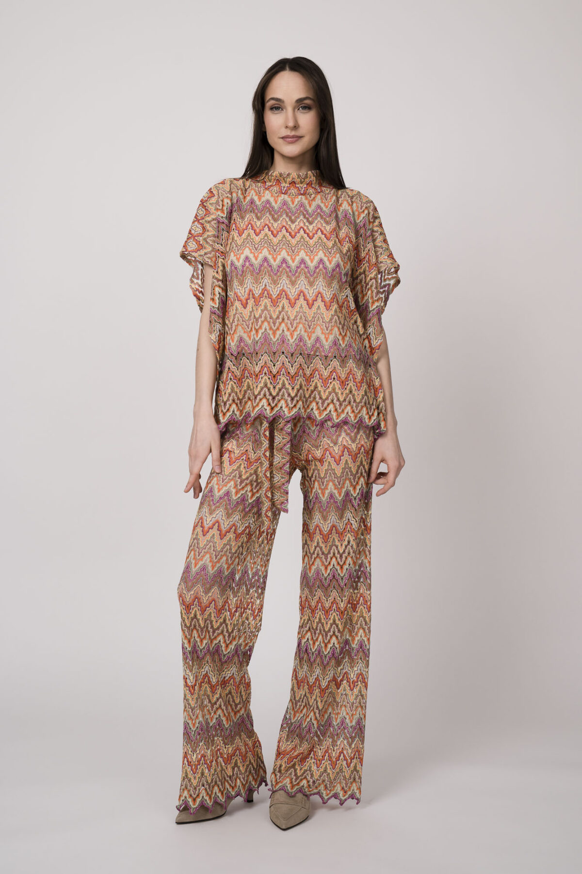 Model trägt ein oranges gemustertes, Strickoberteil und eine dazu passende Strickhose von Ana Alcazar.