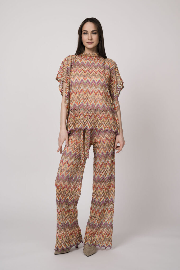 Model trägt ein oranges gemustertes, Strickoberteil und eine dazu passende Strickhose von Ana Alcazar.