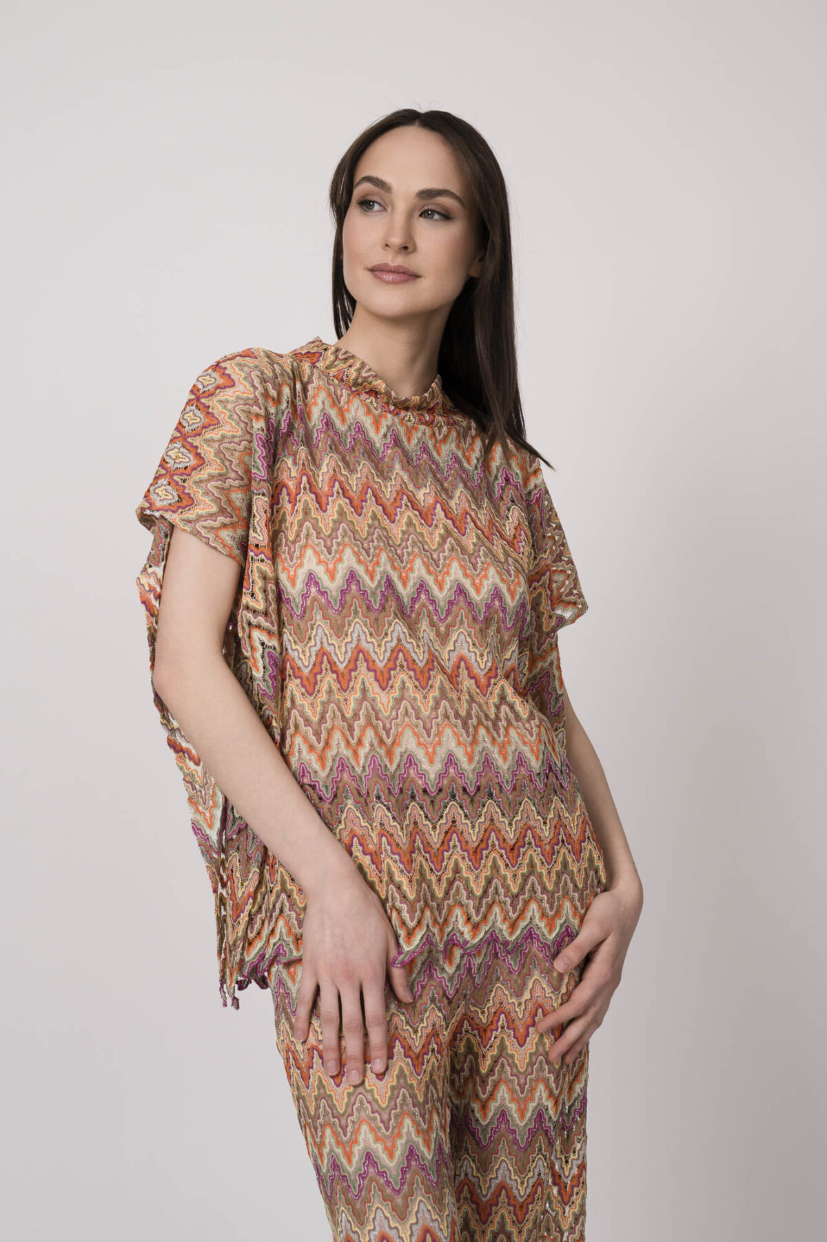 Model trägt ein oranges gemustertes, Strickoberteil von Ana Alcazar.