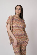 Model trägt ein oranges gemustertes, Strickoberteil von Ana Alcazar.