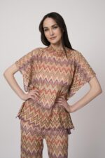 Model trägt ein oranges gemustertes, Strickoberteil von Ana Alcazar.