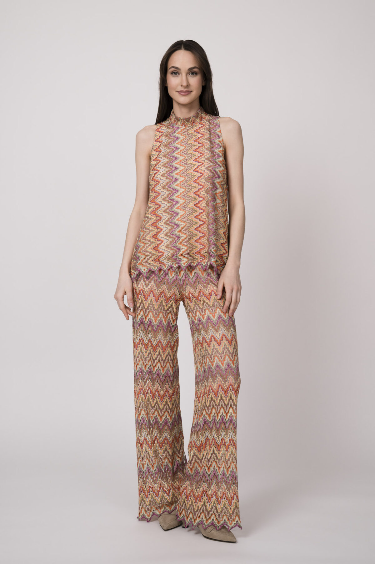 Model trägt ein oranges gemustertes, Strickoberteil und eine dazu passende Strickhose von Ana Alcazar.