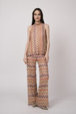 Model trägt ein oranges gemustertes, Strickoberteil und eine dazu passende Strickhose von Ana Alcazar.