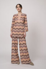 Model trägt ein oranges gemustertes, Strickoberteil und eine dazu passende Strickhose von Ana Alcazar.