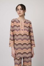 Model trägt ein oranges gemustertes, Strickoberteil von Ana Alcazar.