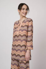 Model trägt ein oranges gemustertes, Strickoberteil von Ana Alcazar.