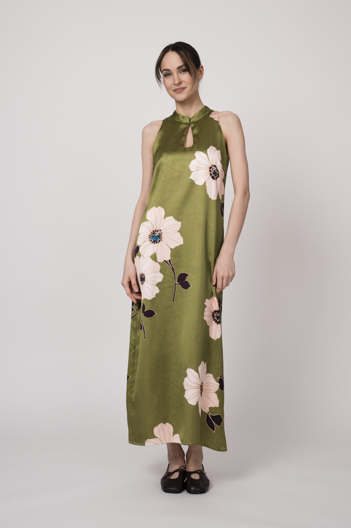 Model trägt ein ärmelloses grünes Kleid mit hellen großen Blumenprints der Marke Ana Alcazar.