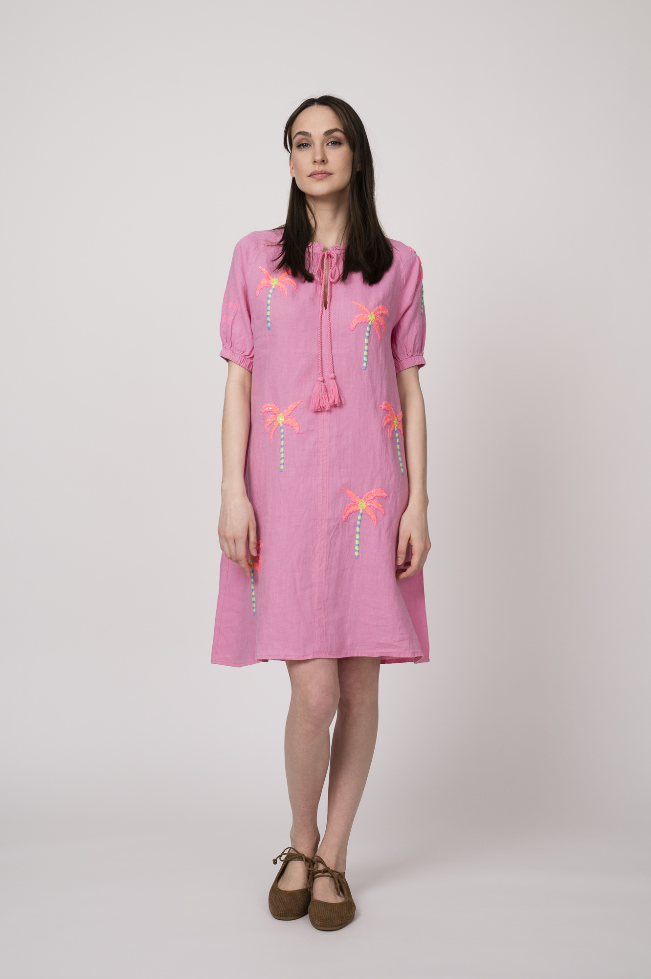 Model trägt ein pinkes kurzes Kleid mit Palmen-Stickereien der Marke Grace.