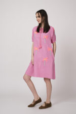 Model trägt ein pinkes kurzes Kleid mit Palmen-Stickereien der Marke Grace.