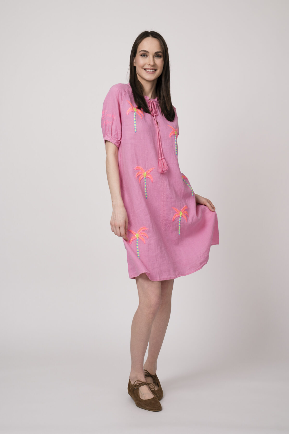 Model trägt ein pinkes kurzes Kleid mit Palmen-Stickereien der Marke Grace.