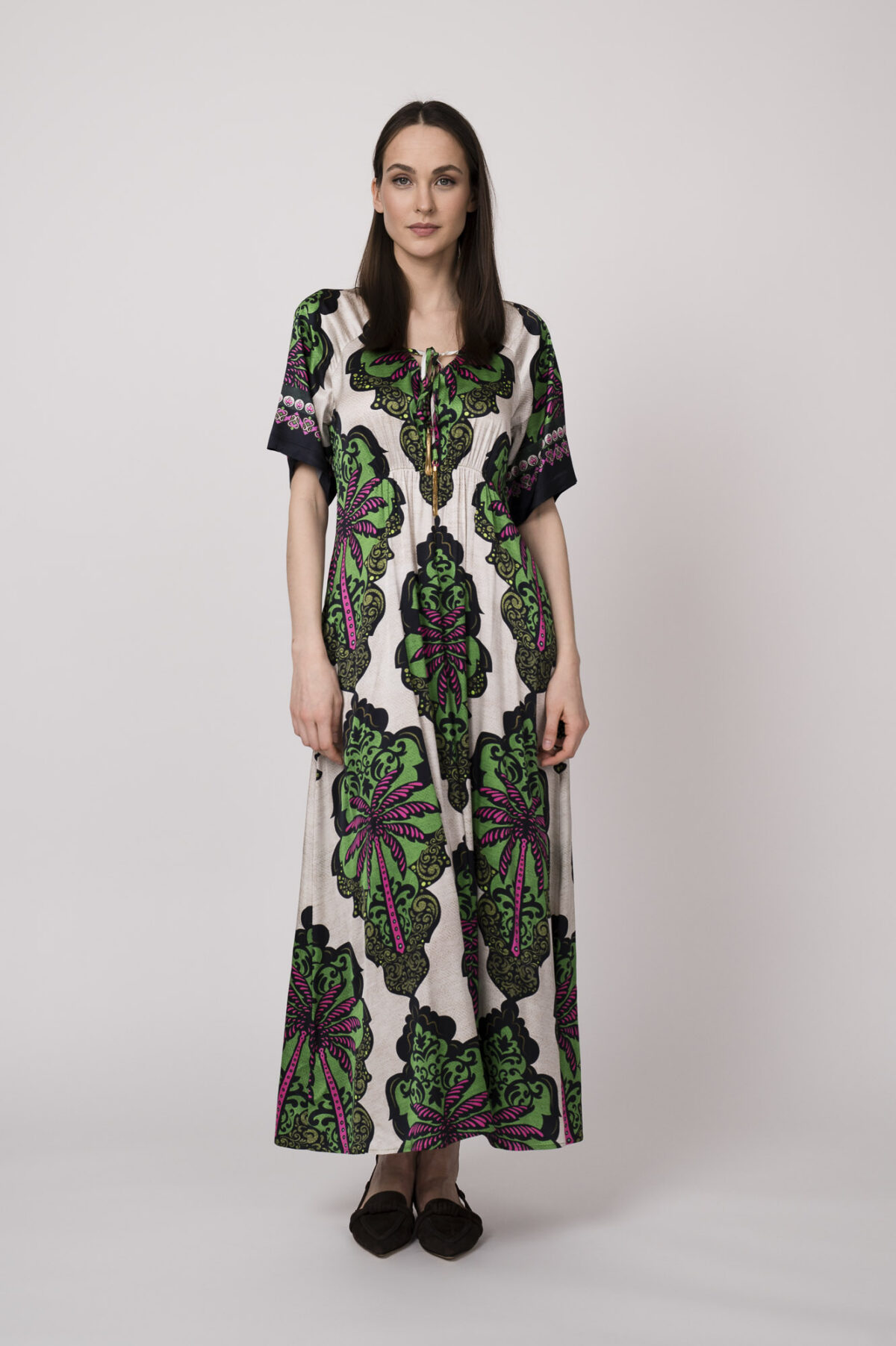 Model trägt ein beiges Kleid mit grün-pinken Ornamenten der Marke Grace.