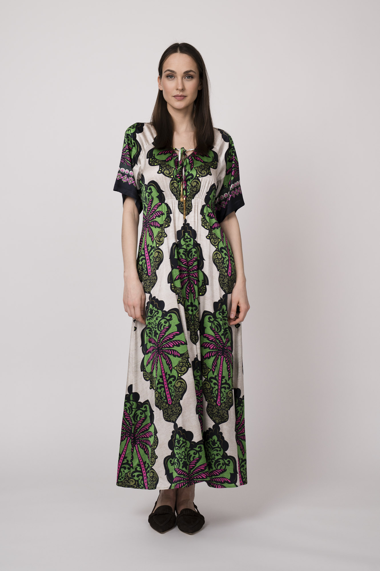 Model trägt ein beiges Kleid mit grün-pinken Ornamenten der Marke Grace.