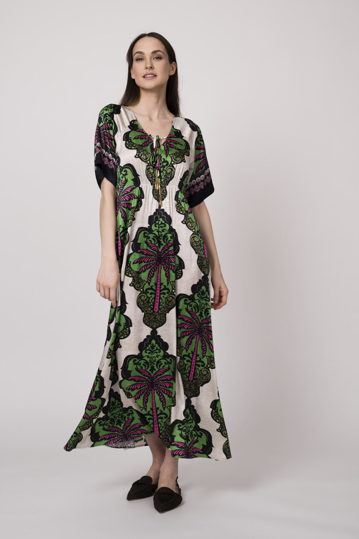 Model trägt ein beiges Kleid mit grün-pinken Ornamenten der Marke Grace.