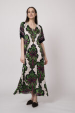 Model trägt ein beiges Kleid mit grün-pinken Ornamenten der Marke Grace.