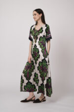 Model trägt ein beiges Kleid mit grün-pinken Ornamenten der Marke Grace.
