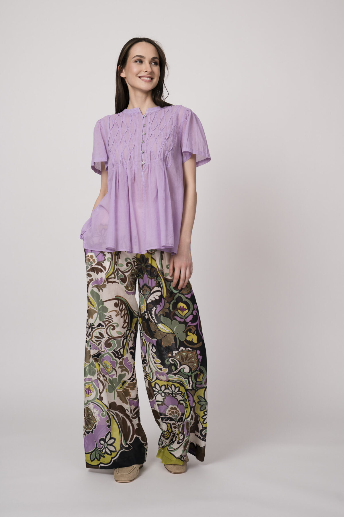 Model trägt eine flieder-farbige Bluse und eine bunte Hose der Marke Devotion.