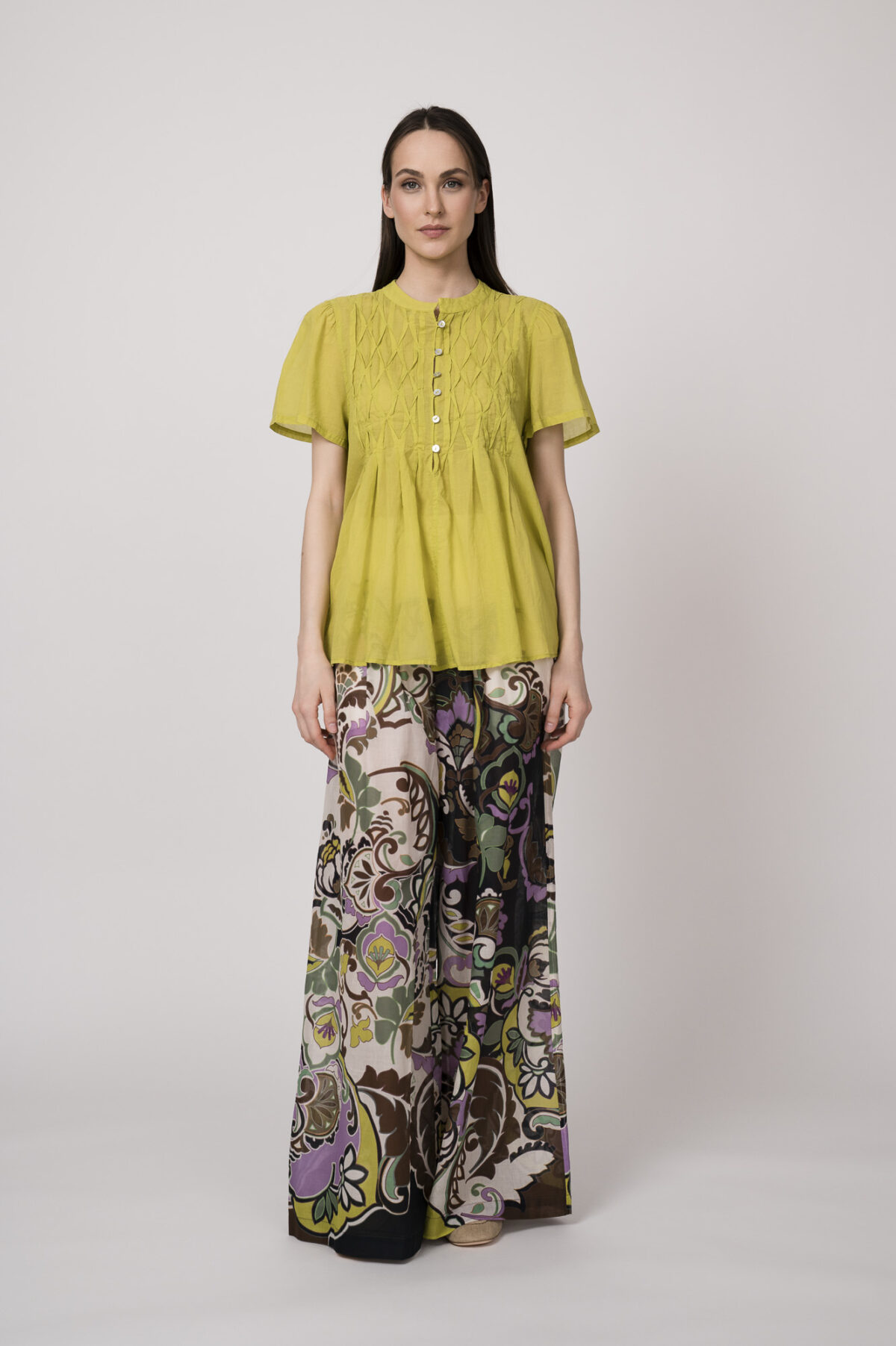 Model trägt eine kiwi-farbige Bluse und eine bunte Hose der Marke Devotion.