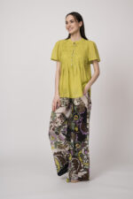 Model trägt eine kiwi-farbige Bluse und eine bunte Hose der Marke Devotion.