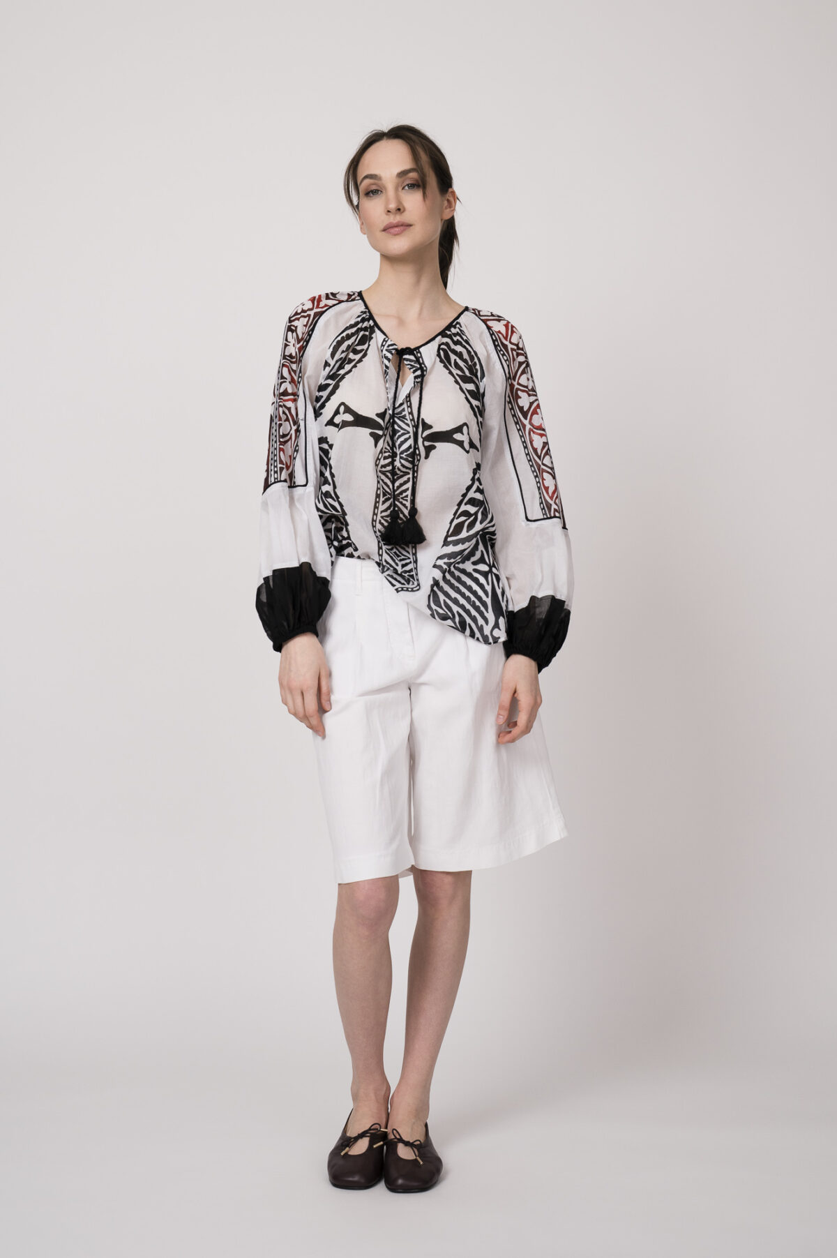 Model trägt eine schwarz-weiß gemustertes Bluse der Marke Devotion und eine Bermuda Shorts der Marke Luisa Cerano.